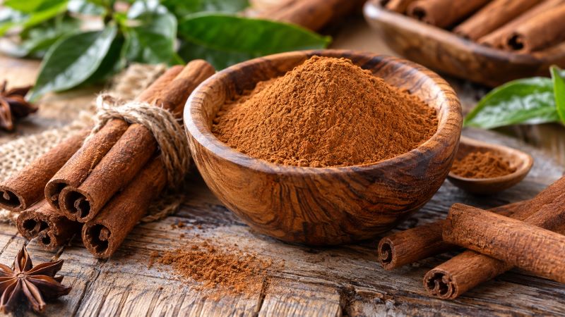 Молотая корица в деревянной миске и палочки корицы на столе